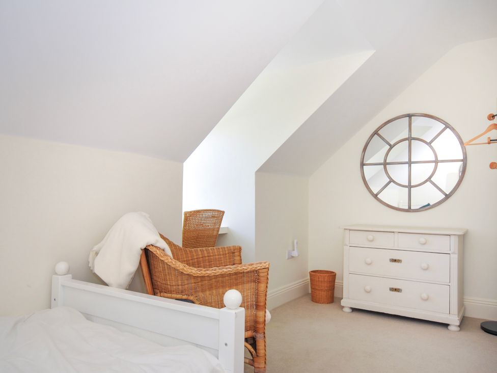 A bedroom with a white bed frame wicker chair white dresser and round mirror at Lowenna Manor 3 in Rock