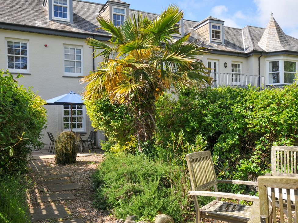 A garden with wooden chairs a stone path and a patio with a table and umbrella at Lowenna Manor 3 Rock