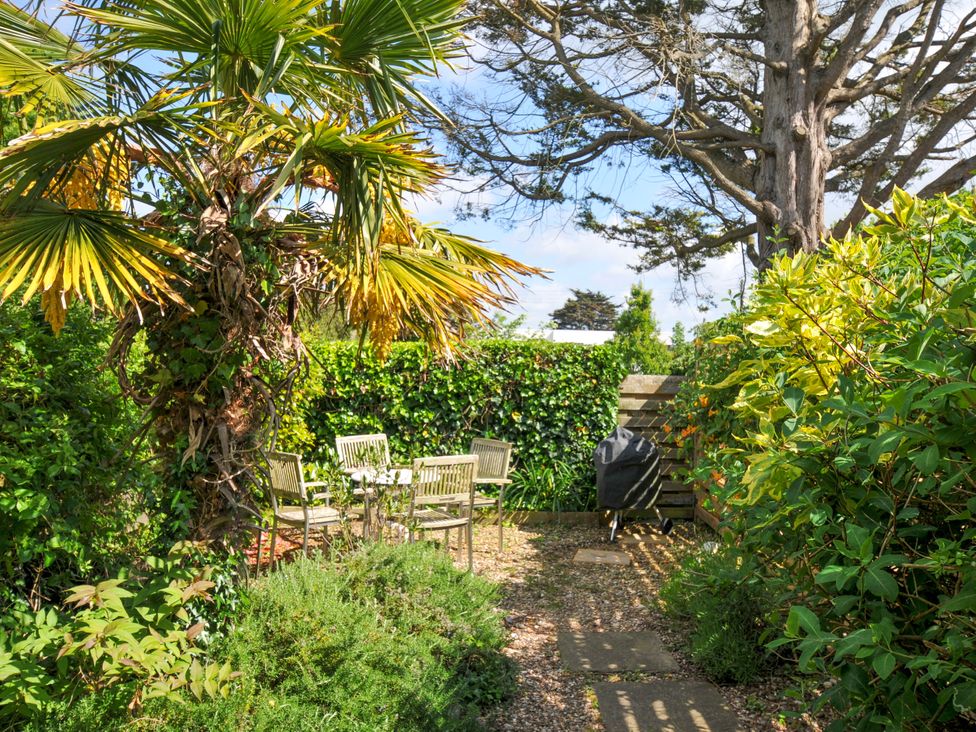 An outdoor patio area with a table and four chairs surrounded by green plants and trees at Lowenna Manor 3 in Rock
