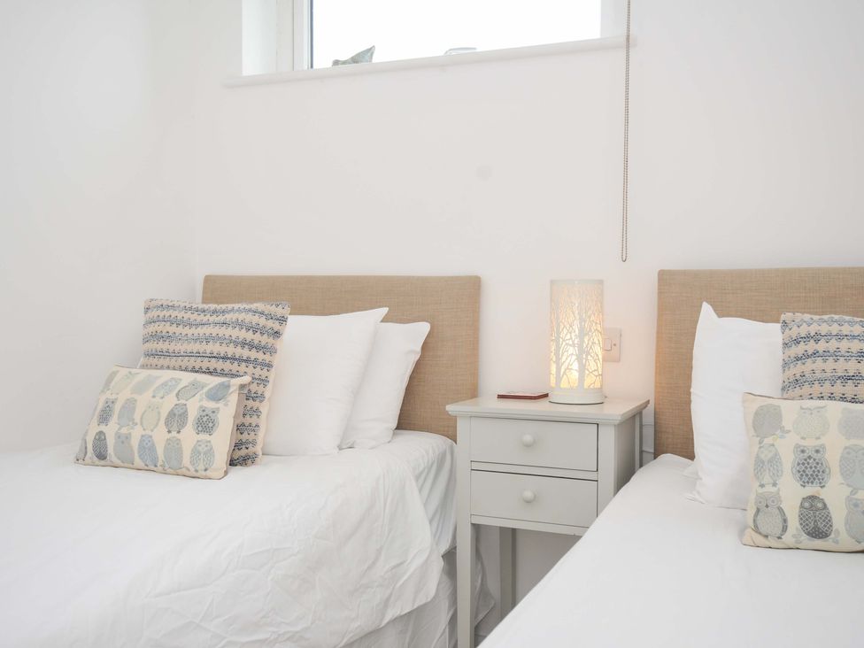 A bedroom with two beds and a lamp on a bedside table at Stepper Point in Polzeath