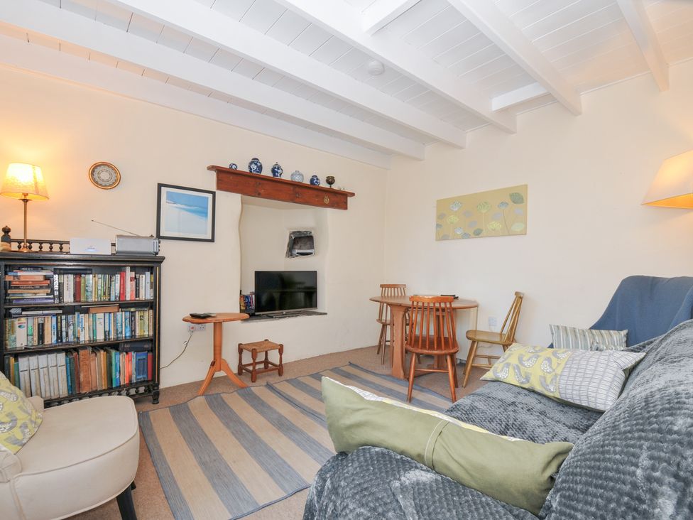 A living room with a sofa and bookshelf at Coppingers Cottage in Polzeath