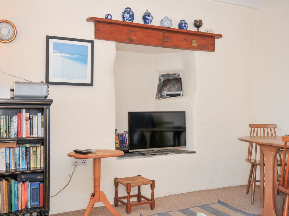 A living room with a bookshelf, television, and table at Coppingers Cottage, Polzeath