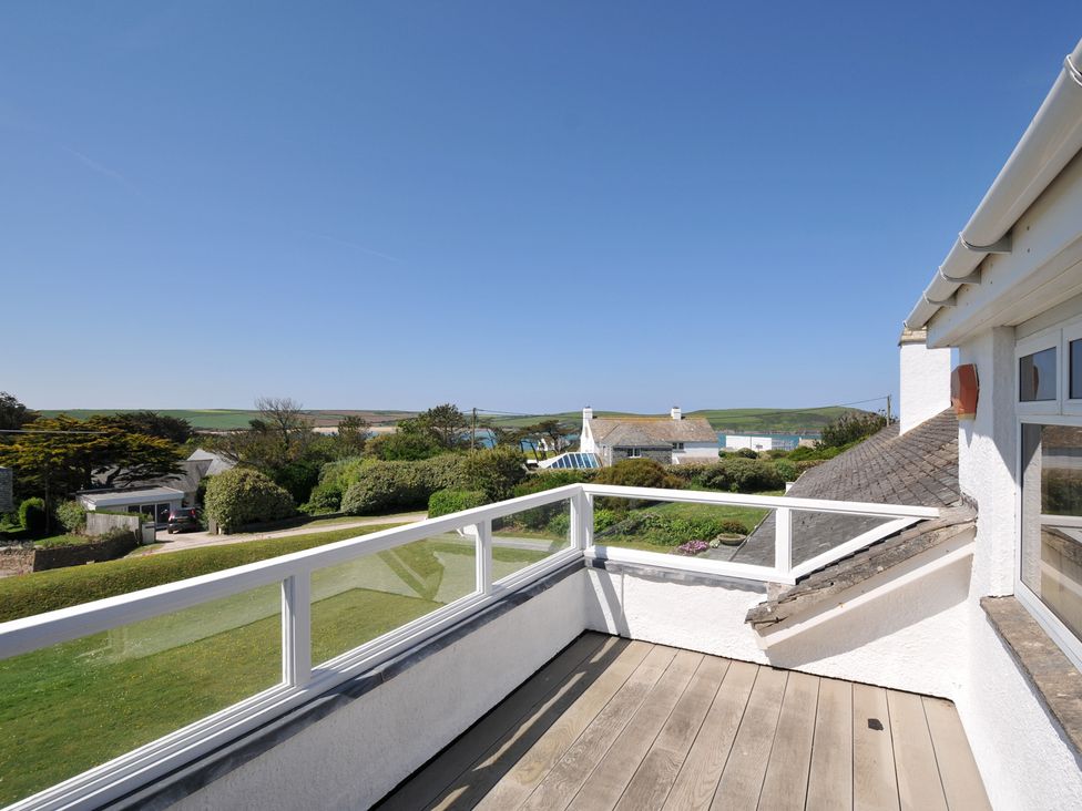 A balcony with glass railing overlooking houses and green fields at Dolphins in Daymer Bay