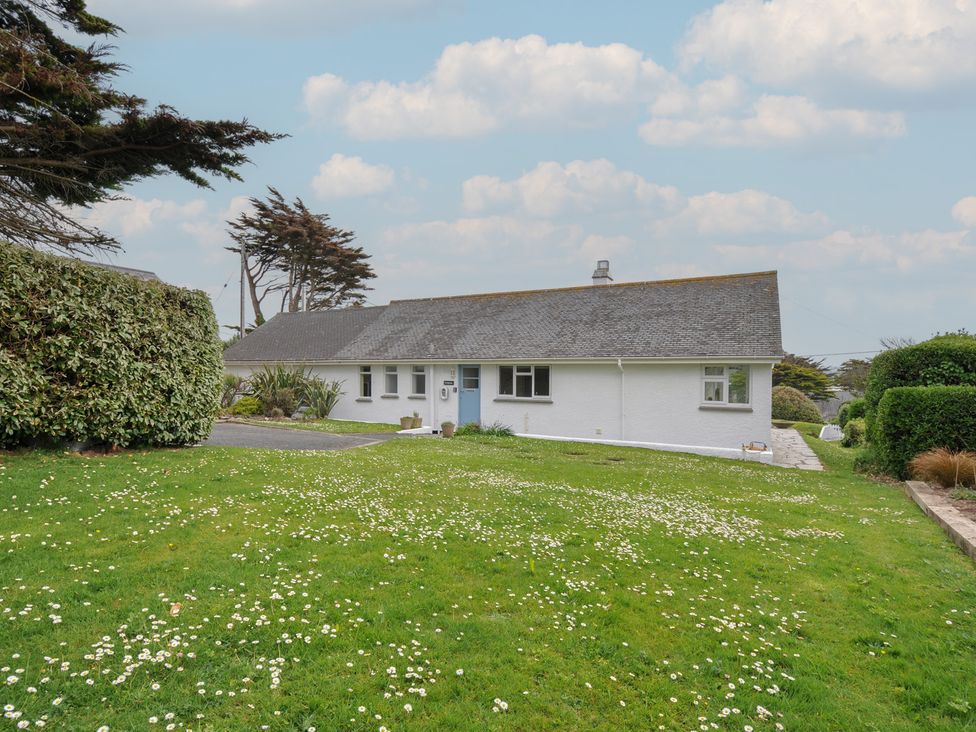 A single story white house with a sloped roof and a front lawn with flowers at Dolphins in Daymer Bay