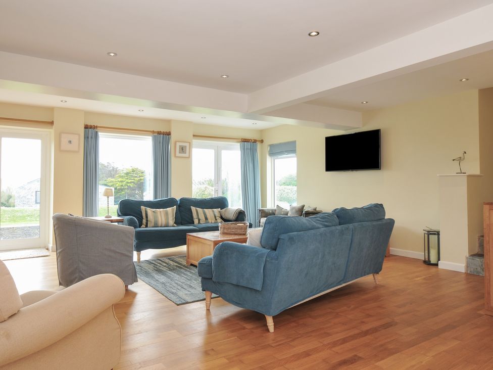 A living room with blue sofas a wooden coffee table and a wall-mounted television at Dolphins in Daymer Bay