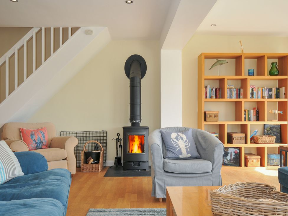 A living room with blue and beige armchairs a wood stove and a wooden bookshelf at Dolphins in Daymer Bay
