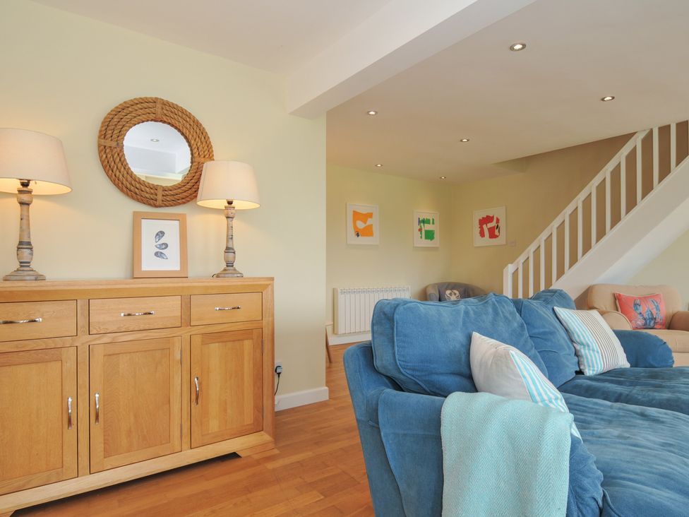 A living room with a blue sofa wooden sideboard with lamps round mirror and framed pictures at Dolphins in Daymer Bay