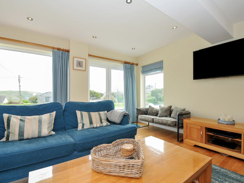 A living room with blue sofa striped cushions wooden coffee table and wall-mounted TV at Dolphins in Daymer Bay