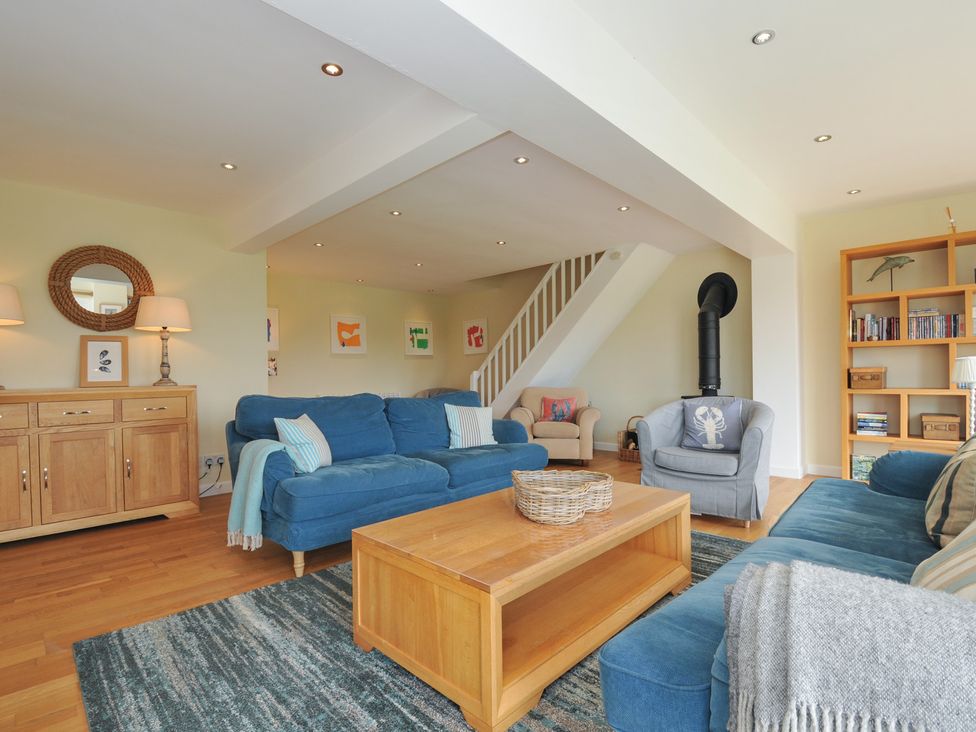 A living room with blue sofas a wooden coffee table a bookshelf and a wood burner at Dolphins in Daymer Bay