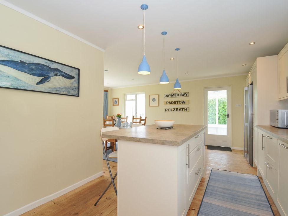 A kitchen with an island and blue pendant lights with a dining area and wall signs at Dolphins in Daymer Bay