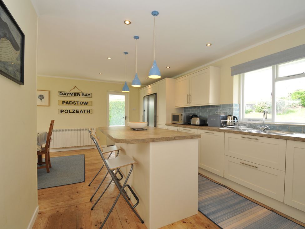 A kitchen with a countertop island with two stools blue pendant lights and kitchen cabinets at Dolphins in Daymer Bay