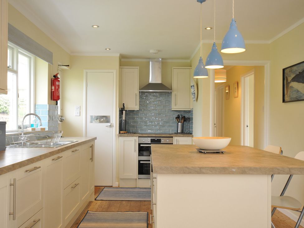 A kitchen with a countertop island and blue pendant lights at Dolphins in Daymer Bay