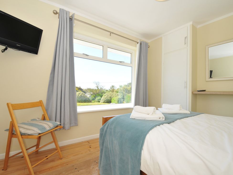 A bedroom with a bed with towels on and a wooden chair with a cushion next to a window at Dolphins in Daymer Bay
