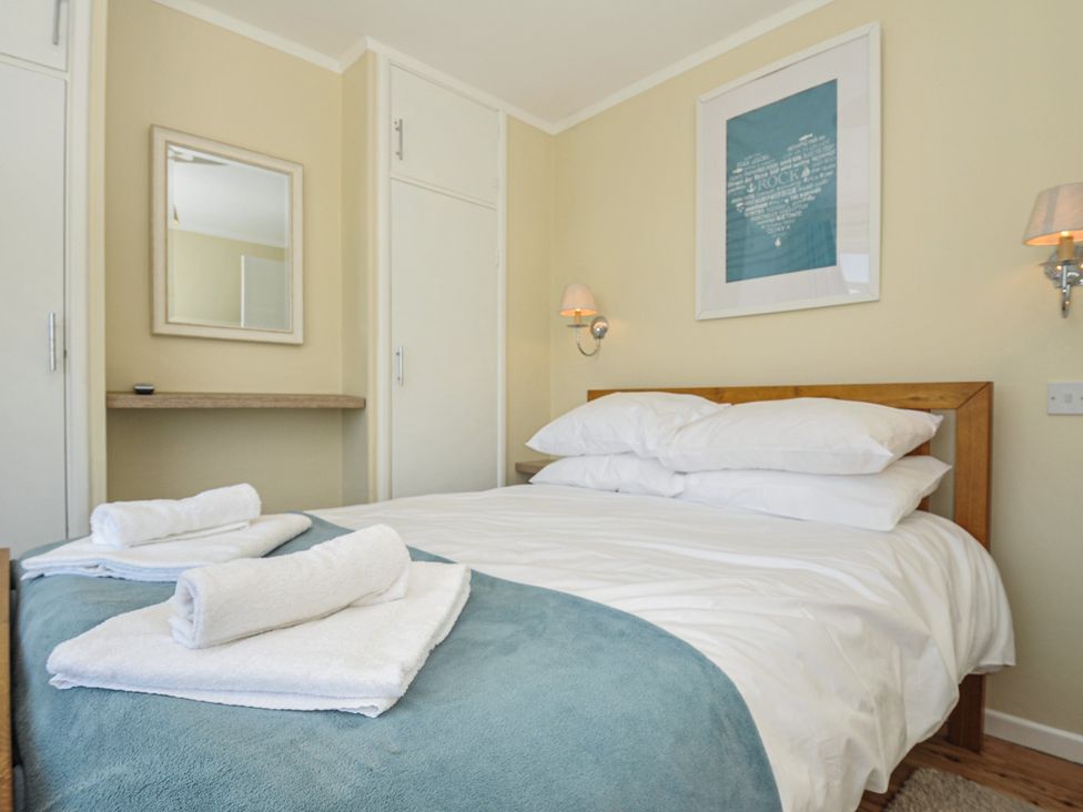 A bedroom with a bed made with white sheets and pillows and a blue blanket with folded white towels on it at Dolphins in Daymer Bay
