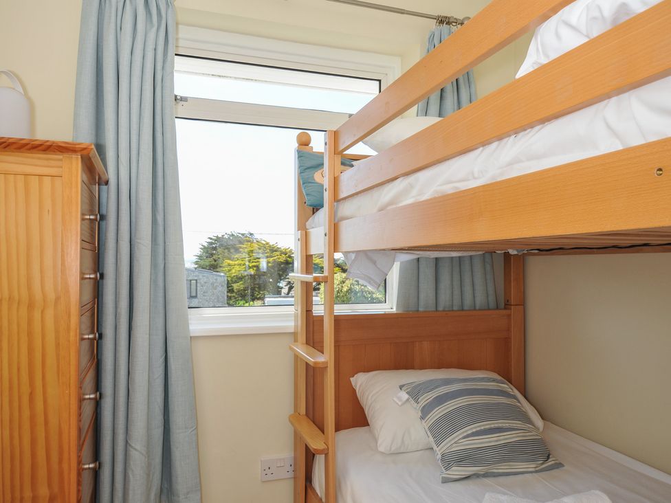 A bedroom with bunk beds near a window and a wooden chest of drawers with blue curtains at Dolphins in Daymer Bay