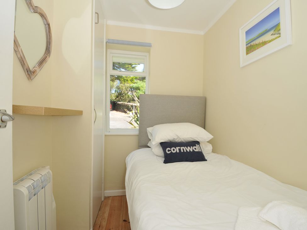 A small bedroom with a single bed a window a wardrobe a mirror and a framed picture at Dolphins Daymer Bay