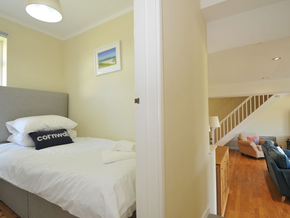 A bedroom with a grey bed and white bedding and a living room with a staircase and armchairs at Dolphins in Daymer Bay