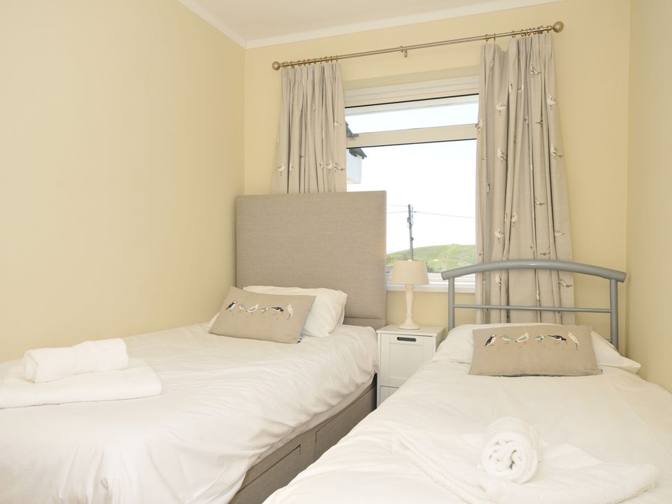 A bedroom with two single beds with white bedding and bird decorated cushions at Dolphins in Daymer Bay