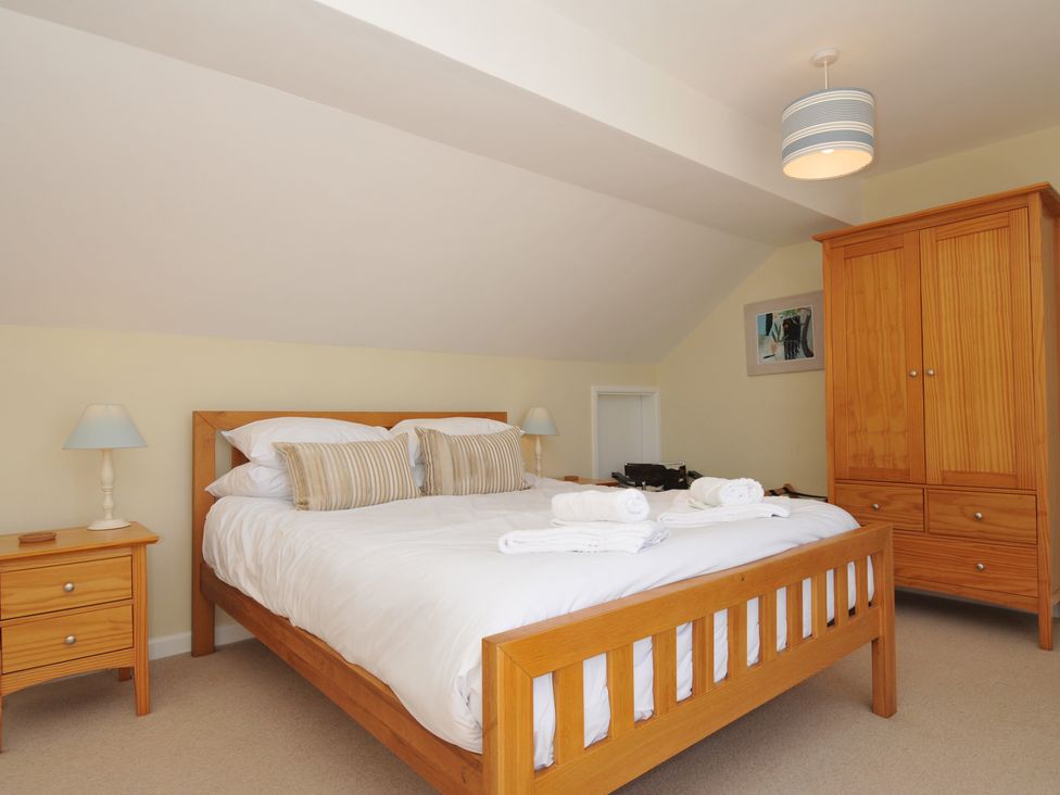 A bedroom with a wooden bed with white bedding and folded towels two bedside tables with lamps a wooden wardrobe and a ceiling light at Dolphins in Daymer Bay