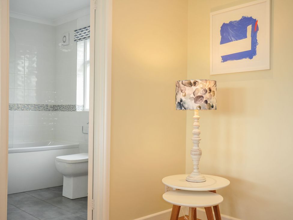 A corner of a room with a lamp on nested tables and a view into a bathroom with a bathtub and toilet at Dolphins in Daymer Bay