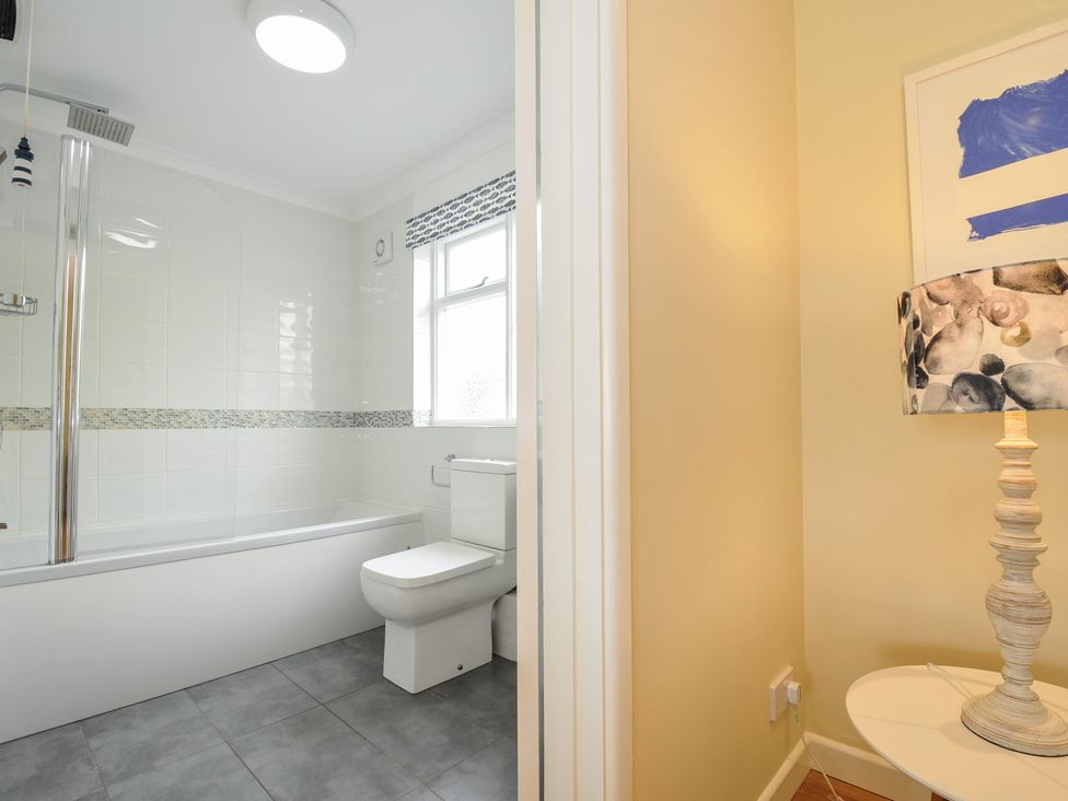A bathroom with a bathtub shower and toilet beside a room corner with a table lamp at Dolphins in Daymer Bay