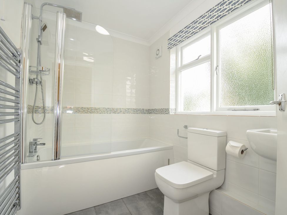 A bathroom with a bathtub shower combination toilet sink and window at Dolphins in Daymer Bay