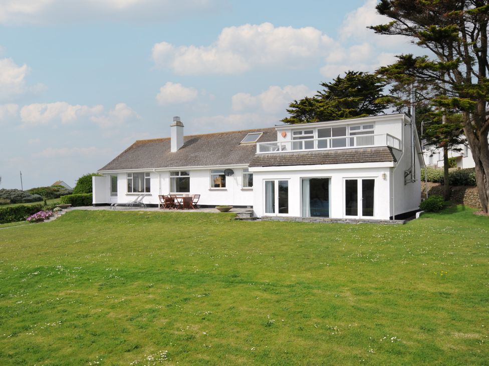 A white house with large windows and a grassy lawn surrounded by trees at Dolphins in Daymer Bay