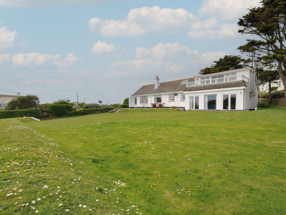 A white house with large windows and a balcony in a green yard with scattered flowers and trees at Dolphins in Daymer Bay