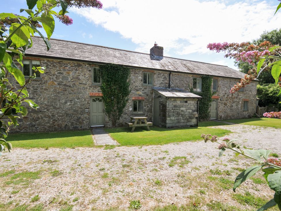 A stone house with a table and bench in the garden at Orchard Cottage in Polzeath