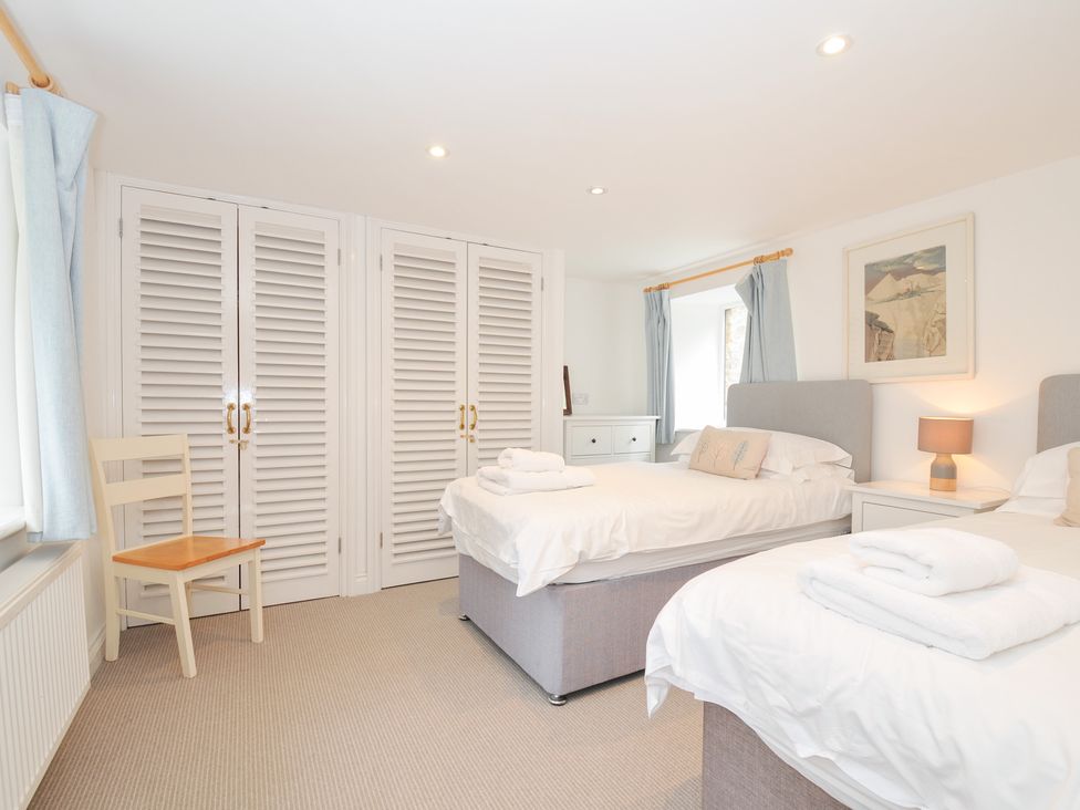 A bedroom with two beds and a chair at Orchard Cottage in Polzeath