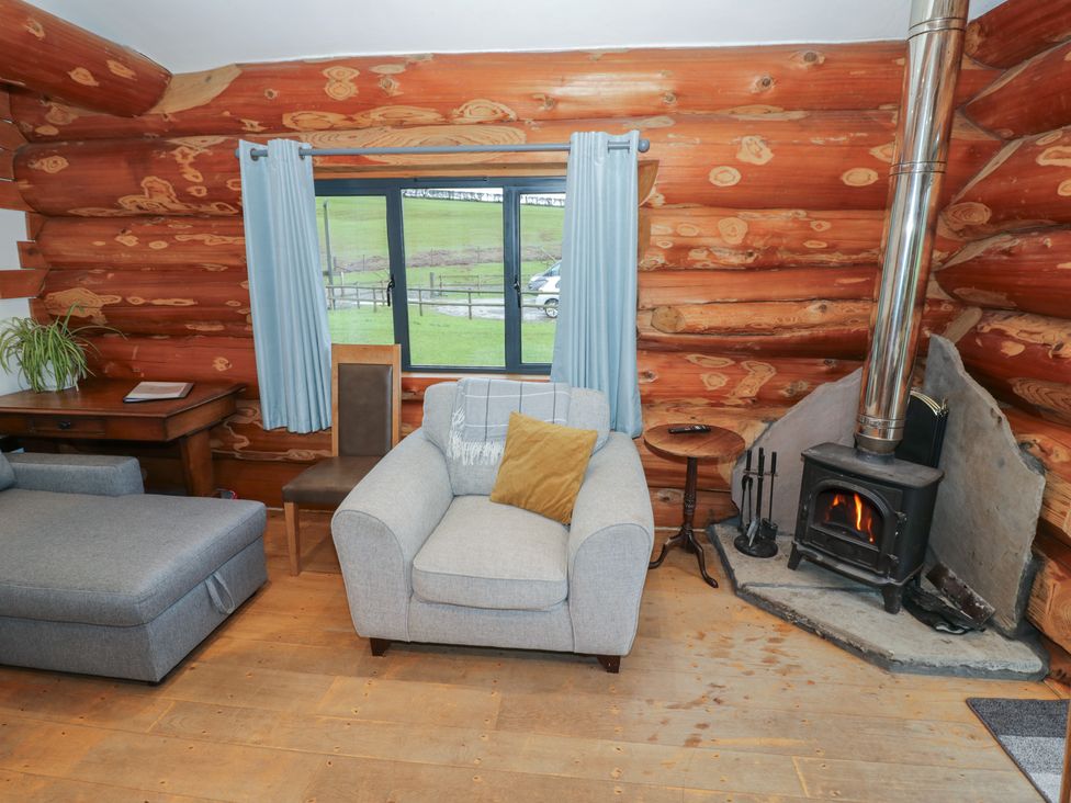 A living room with a sofa, armchair, and stove at Cedar Cabin at Salford Court Farm Fishing Cabins near Clifton Upon Teme