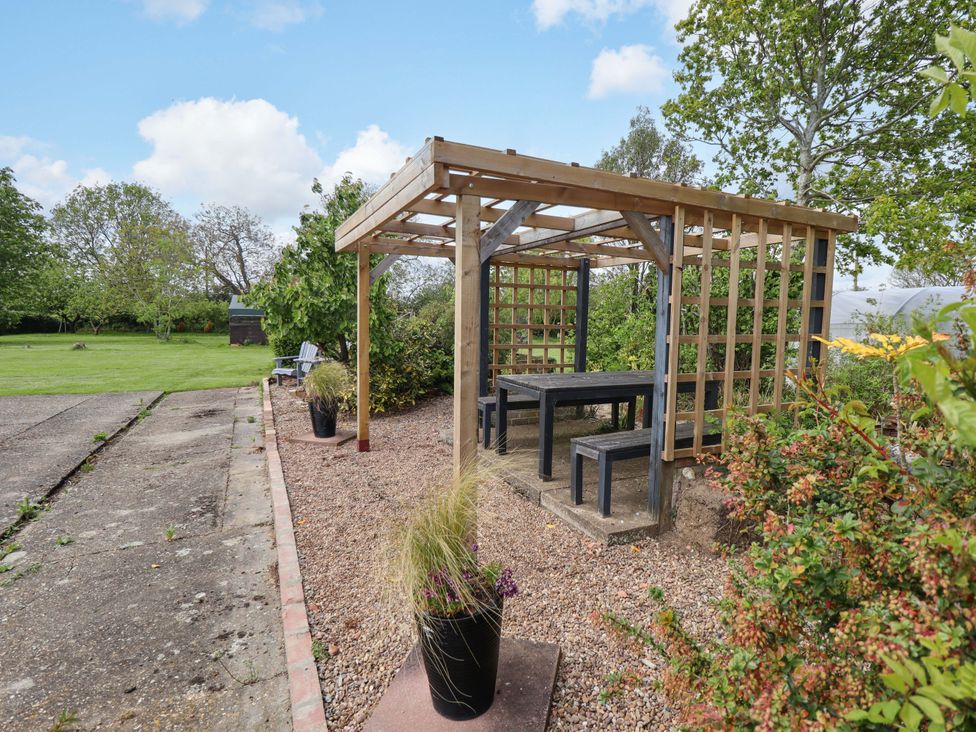 A pergola with a table and benches surrounded by gravel and plants at The New Build in South Reston near Louth