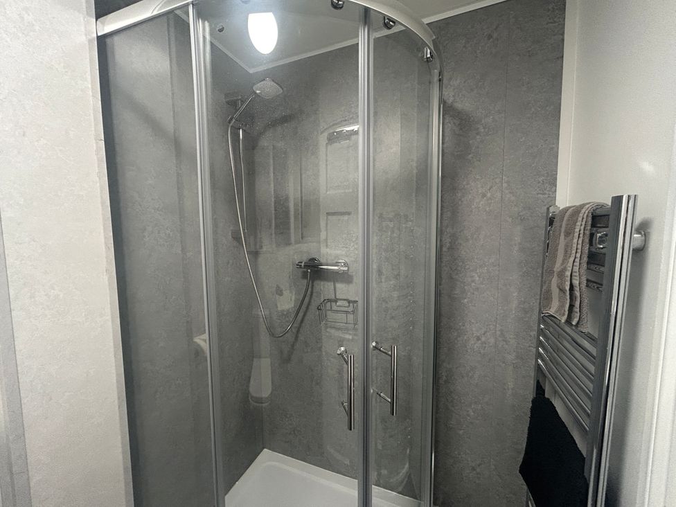 A shower enclosure with glass doors and towel warmer at Solway Firth View in Powfoot near Annan
