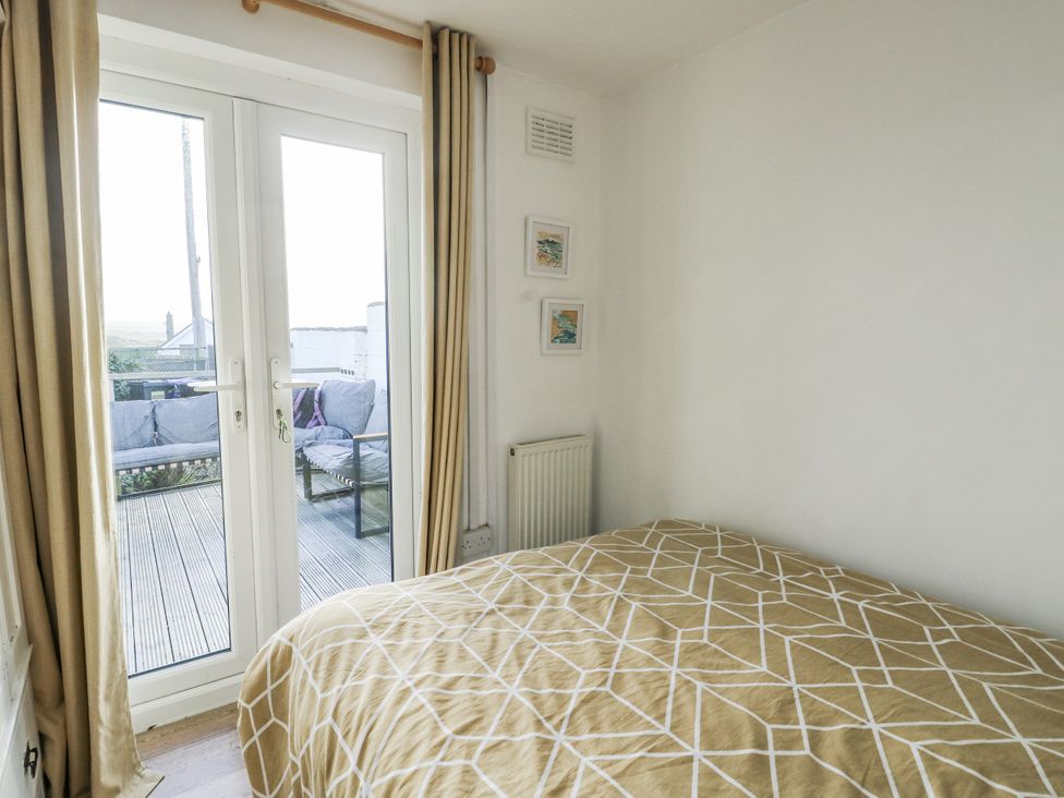 A bedroom with a bed and double doors leading to outdoor seating at 7 Bro Branwen Aberffraw near Rhosneigr