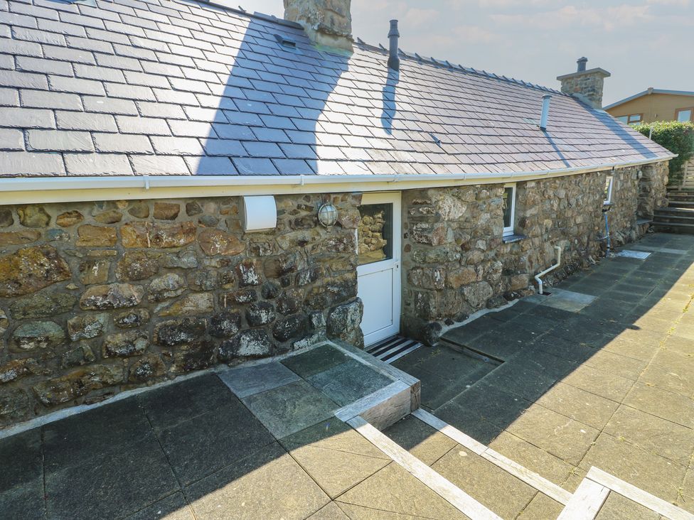 An outdoor area with a stone wall and door at Sunstone (Garreg Haul) Cilan near Abersoch