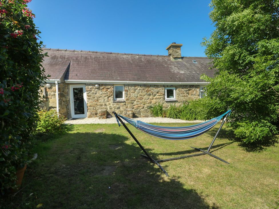 A garden with a hammock in front of a stone cottage at Sunstone (Garreg Haul) Cilan near Abersoch