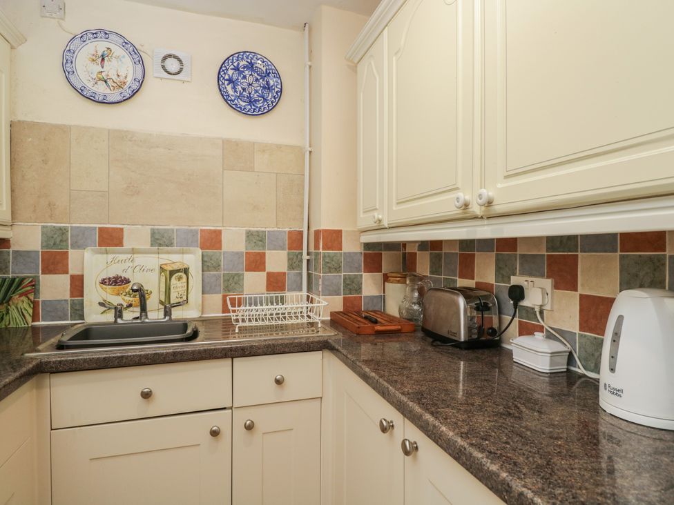 A kitchen with a sink, toaster, kettle, and decorative tiles at Dollar Ward House Basement Cirencester