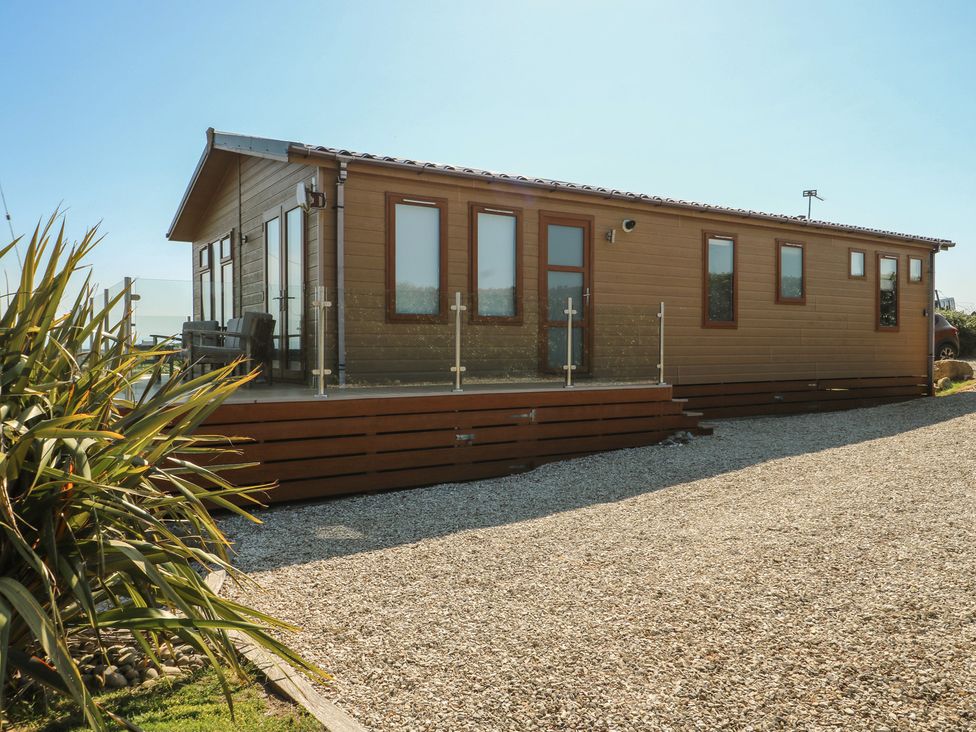 A wooden lodge with windows and decking in an outdoor area at Sunstone Lodge (Garreg Haul Lodge) Cilan near Abersoch
