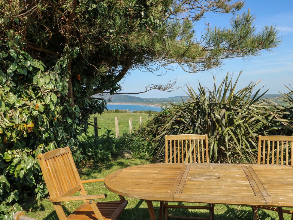 An outdoor dining area with a table and chairs overlooking the sea at Sunstone Lodge (Garreg Haul Lodge) Cilan near Abersoch