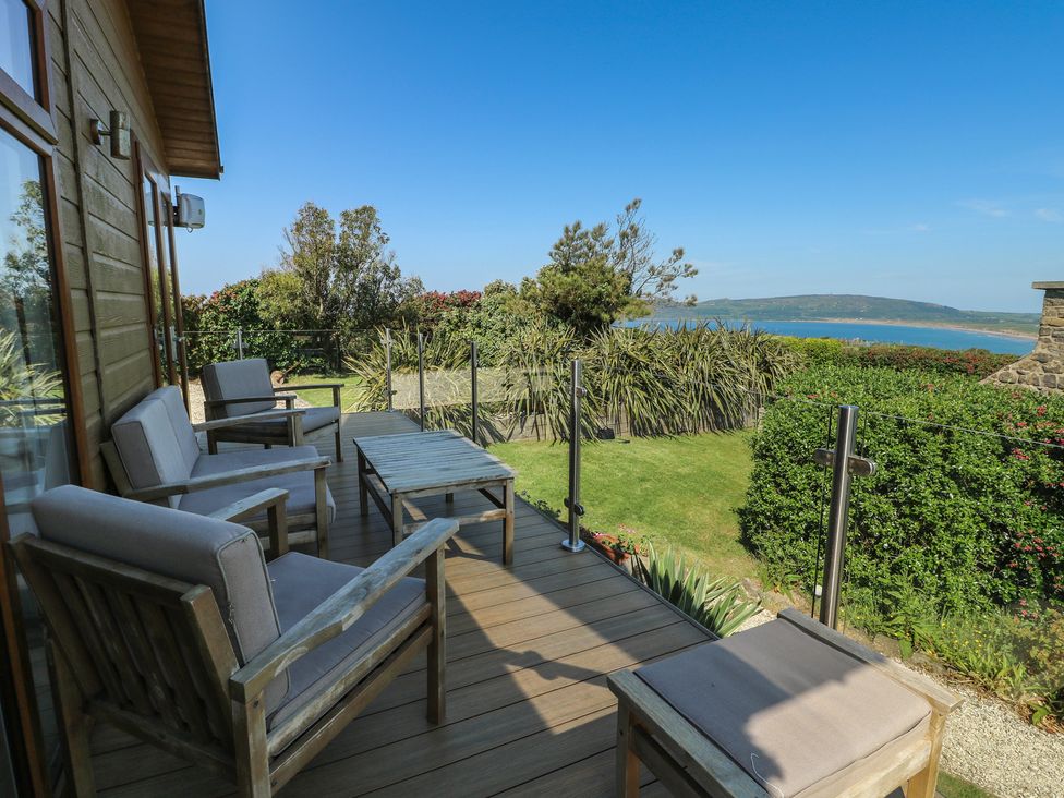 A deck area with wooden chairs and a table at Sunstone Lodge (Garreg Haul Lodge) Cilan near Abersoch