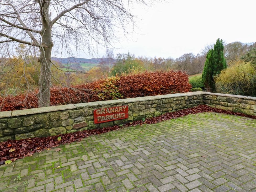 An outdoor parking area with a stone wall and sign at The Granary in Rothbury