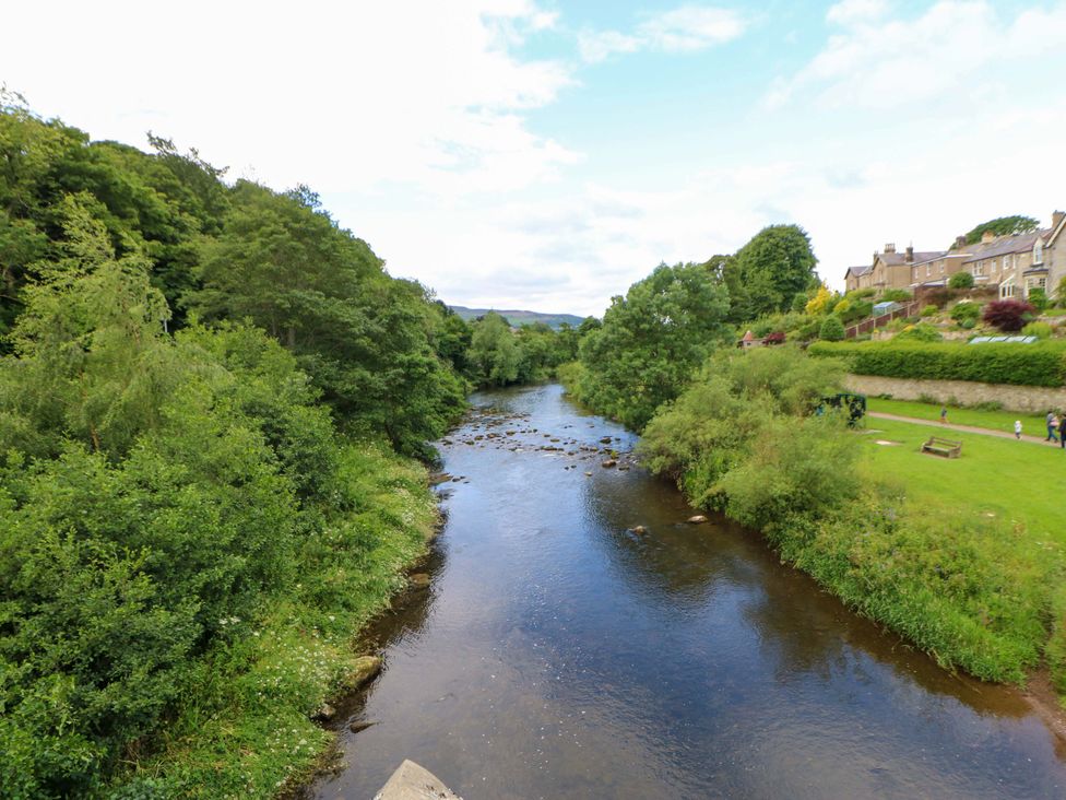 A river with trees and houses along the bank at The Granary in Rothbury