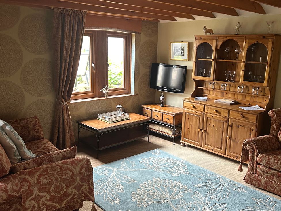 A living room with a sofa, table, television, and sideboard at Swaledale Watch Garden Annexe in Caldbeck