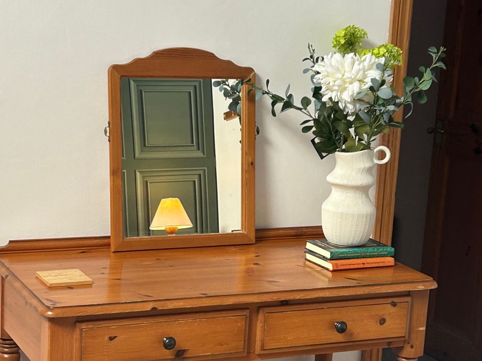 A table with a mirror, lamp, flowers in a vase, and books at Swaledale Watch Garden Annexe, Caldbeck