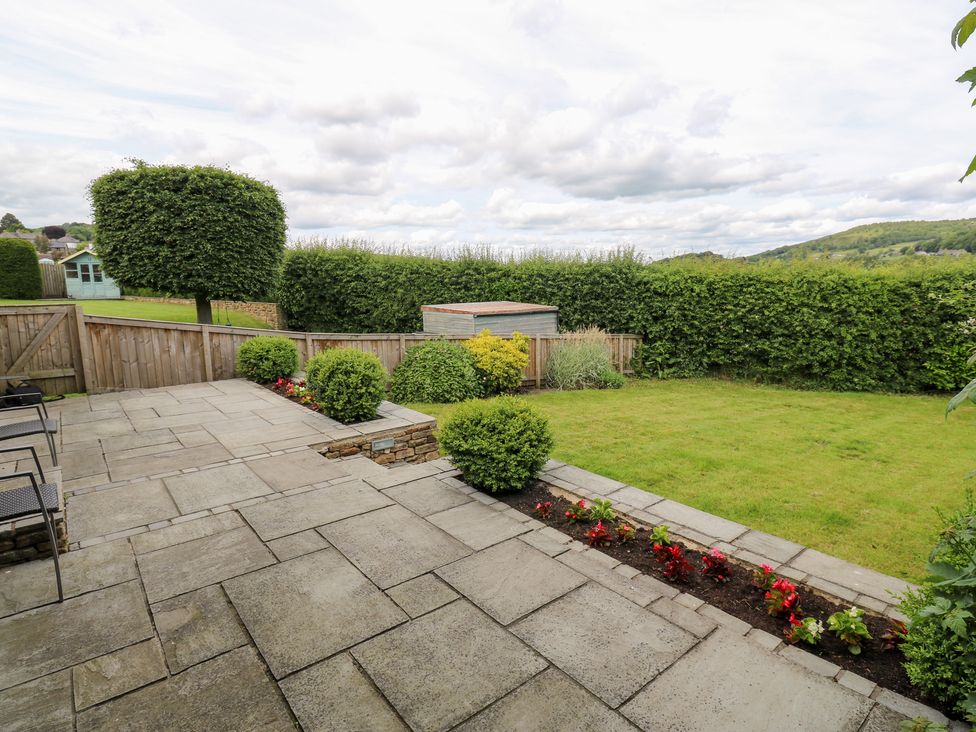 A garden with a patio area, grass, and hedges at Farnhill View in Cross Hills