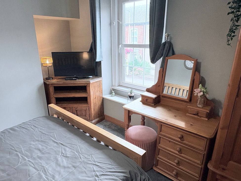 A bedroom with a bed, television, dresser, and pouffe at The Oaks Cottage in Penrith