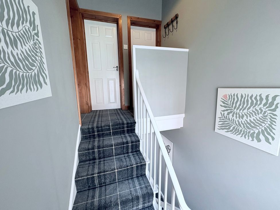A staircase leading to a hallway with doors and wall decorations at The Oaks Cottage in Penrith