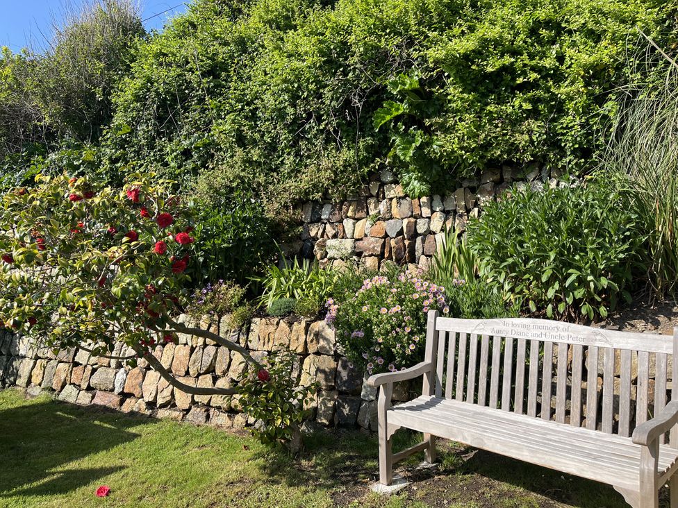 A garden with a stone wall and a wooden bench at Stonecroft in Praa Sands