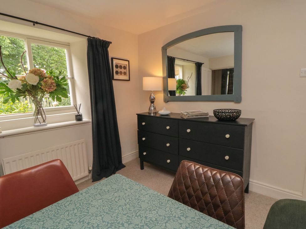 A dining room with a table and flowers on the dresser at Black Horse Cottage in Swainby