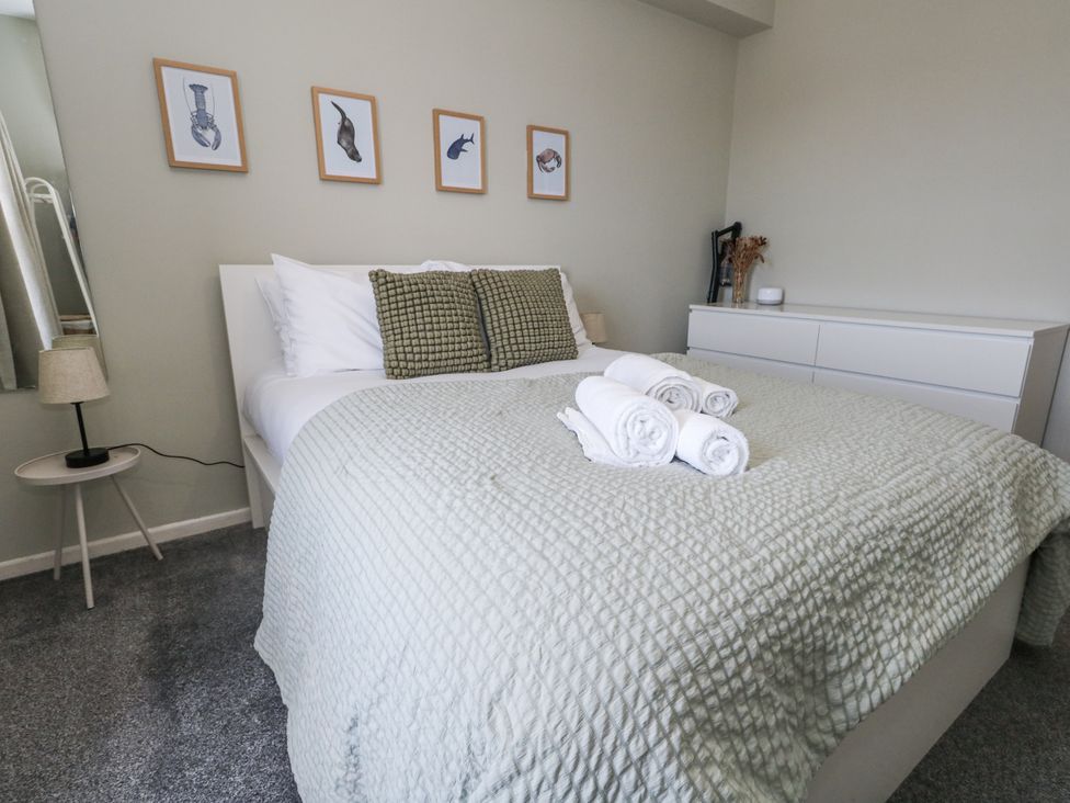A bedroom with a bed, towels, and wall art at Beachcomb in Weymouth